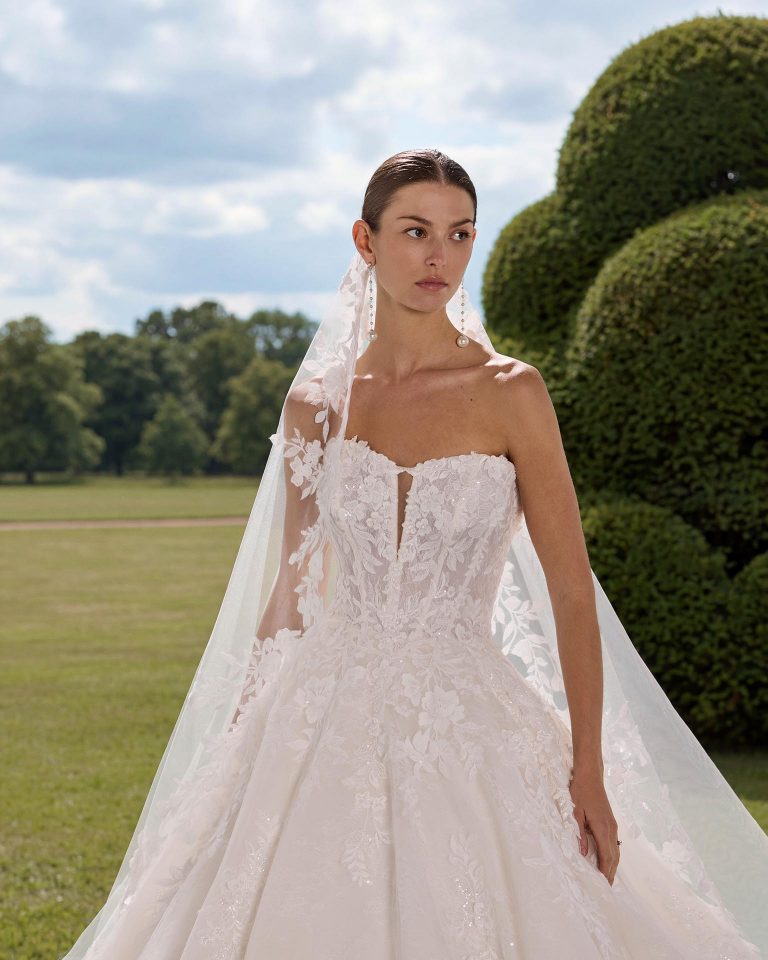 Princess silhouette wedding dress with deep neckline. Lace bodice with beadwork, removable long lace sleeves, corset back. Includes lace choker. LUNA_NOVIAS.