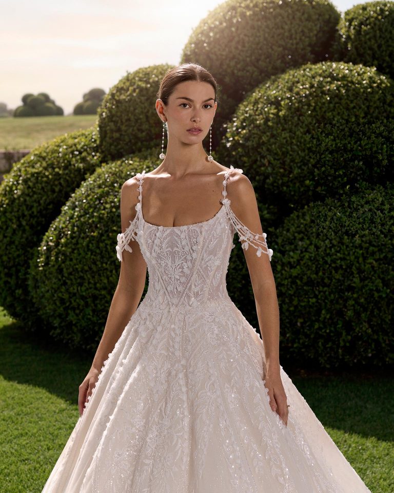Princess silhouette wedding dress with round neckline, straps with floral embellishments, lace beadwork on the bodice and open back. LUNA_NOVIAS.